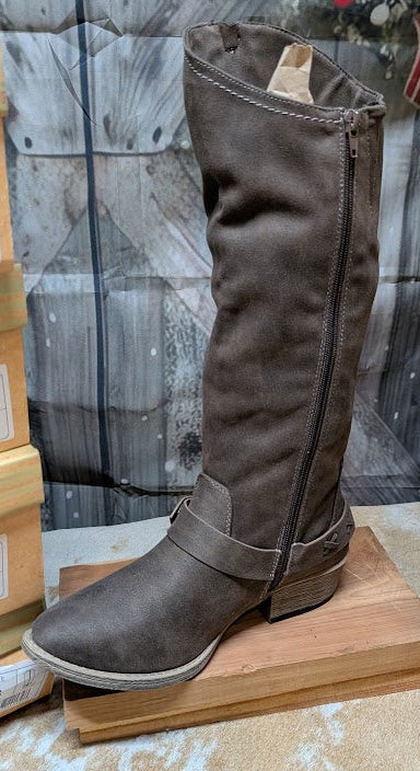 Brown knee-high boot on a wooden block with barn door the background