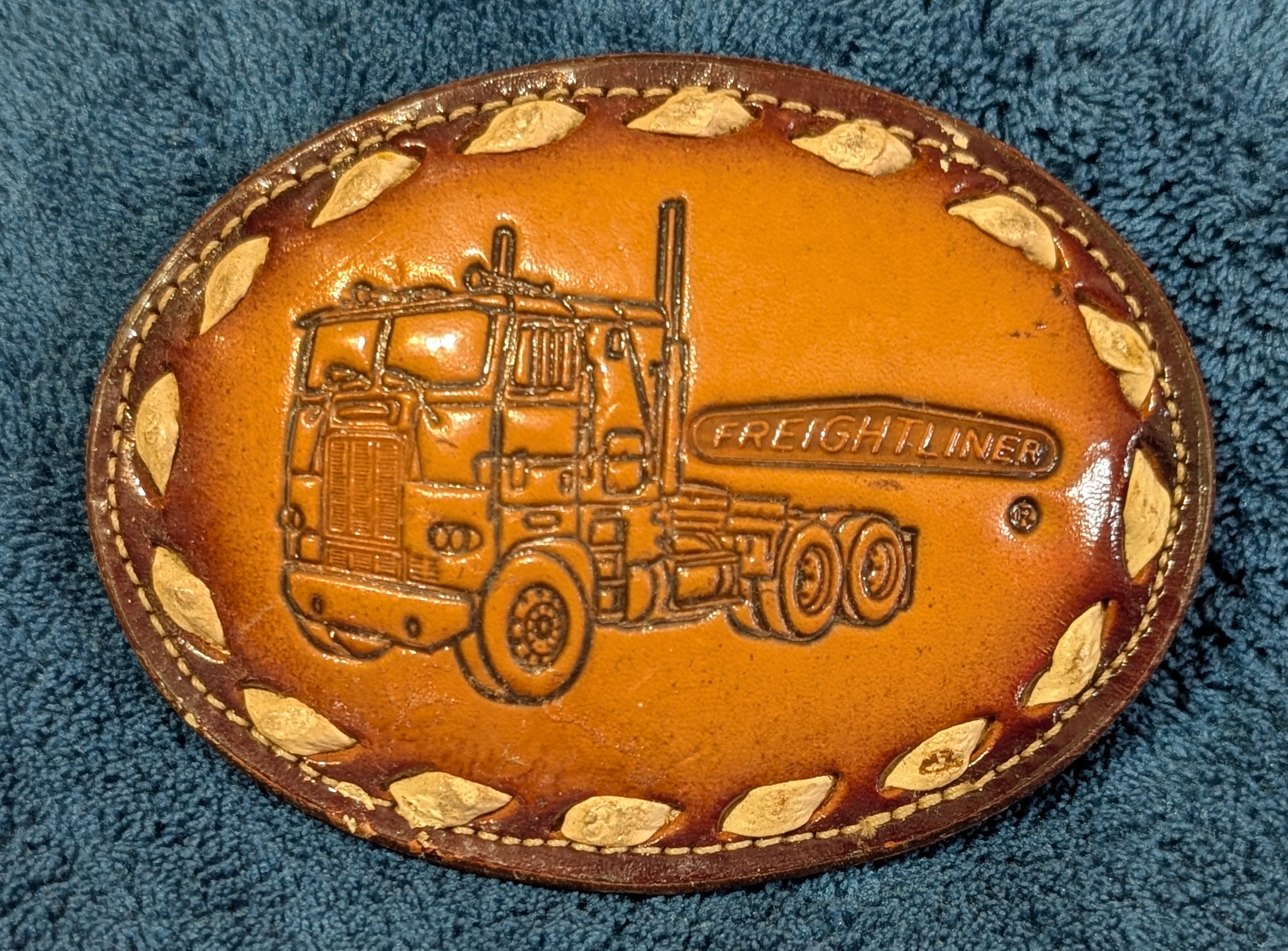 Leather belt buckle with truck design on a blue textured background