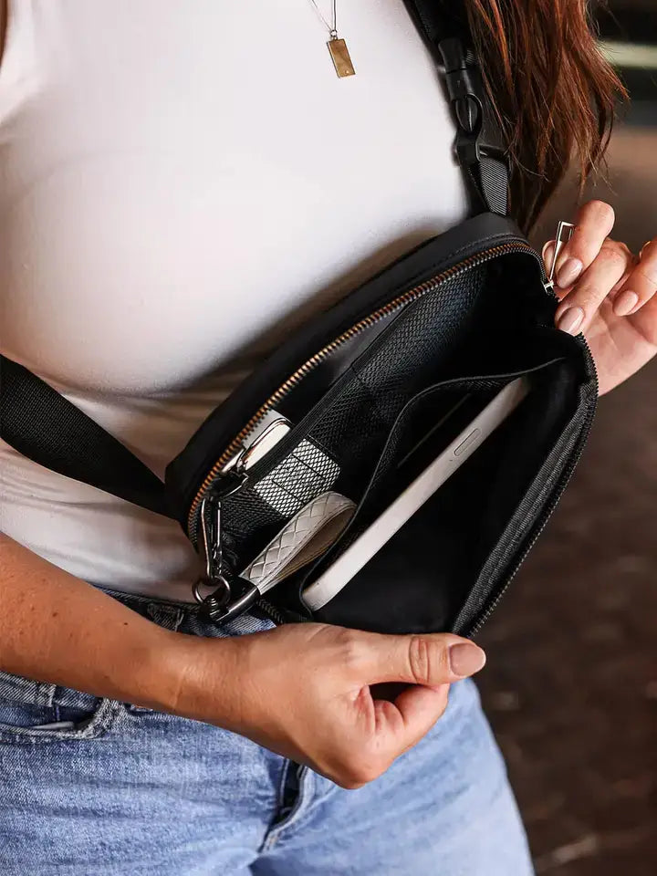 Person holding a black crossbody bag with a white shirt and blue jeans.