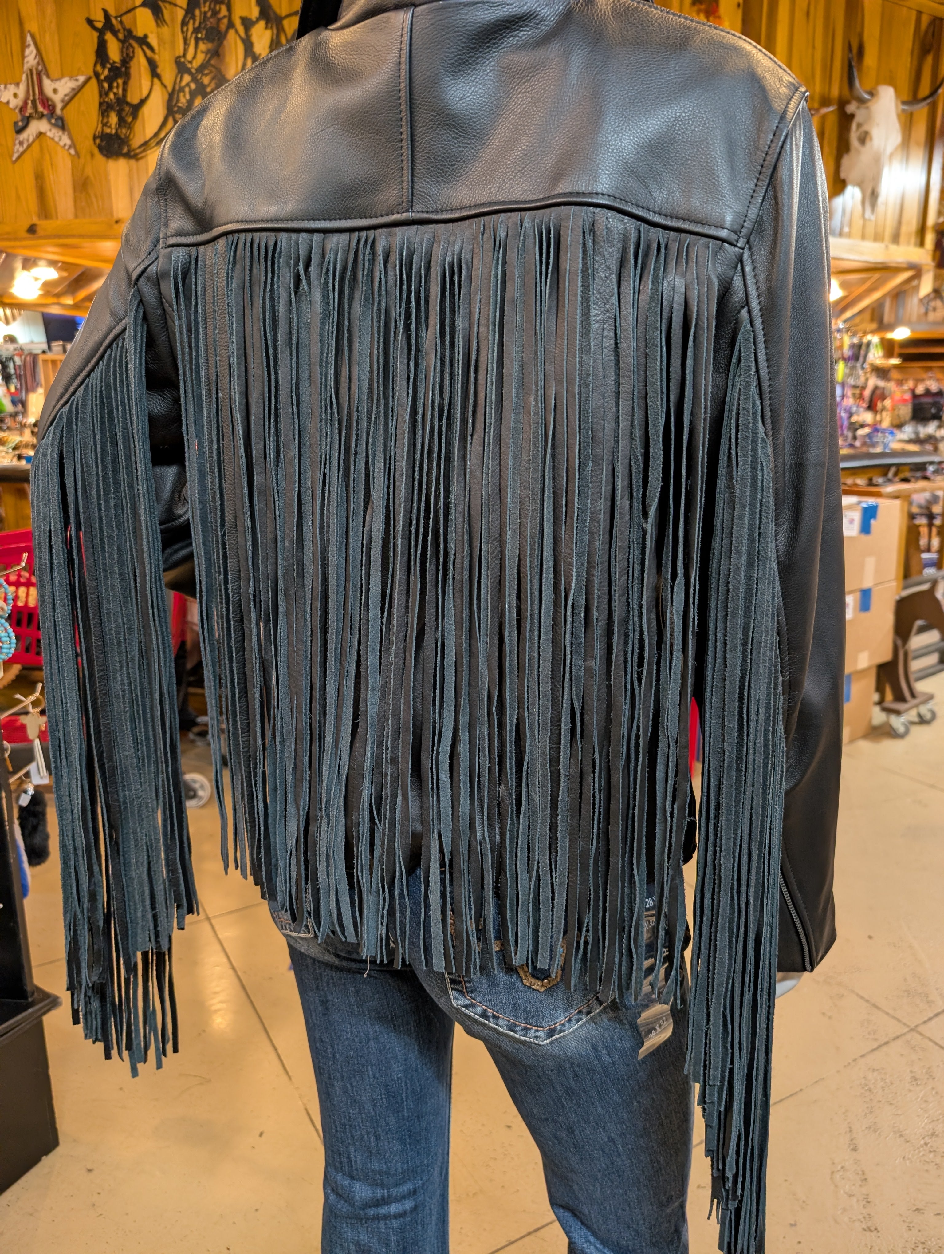 Black leather jacket with fringes worn by a person in an indoor setting