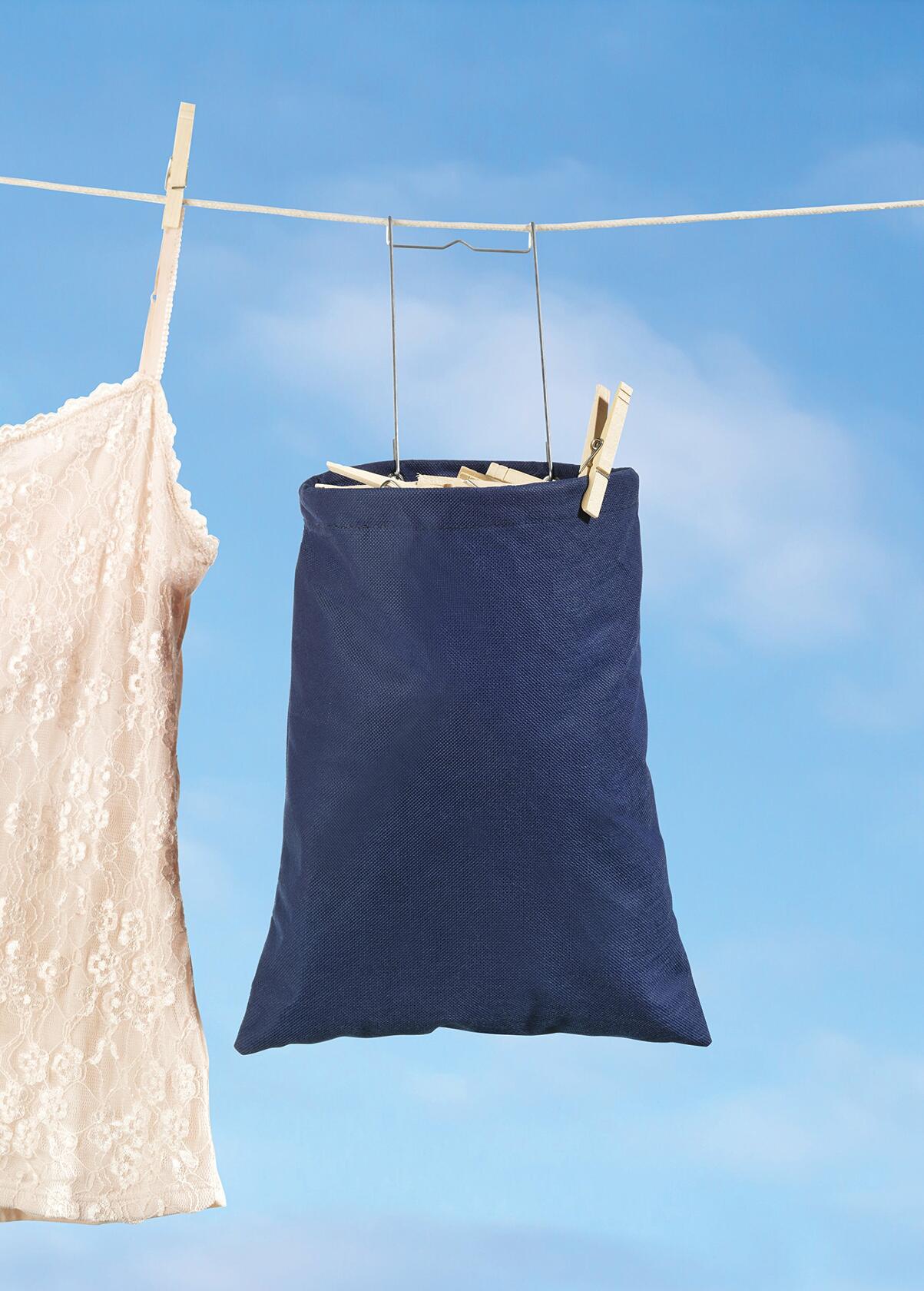 Whitmor clothespin bag filled with pins, hooked on a clothesline during outdoor laundry day