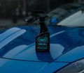 Widow Wax Luxury Leather and Vinyl Protectant 16 oz spray bottle sitting on the hood of a blue sports car.