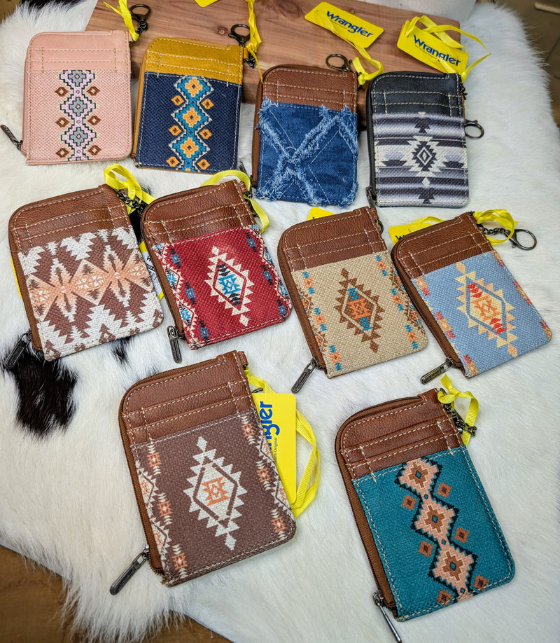 Multiple colors of Wrangler by Montana West Southwestern print mini zip card holders displayed on a white cowhide background.