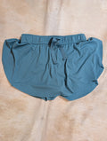 Dusty teal Tennis shorts on a textured rug.