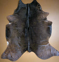 Individually named Dandy a full cowhide rug with a dark brown and black color with snip of white on the edge and natural patterns, laid out on a flat surface.