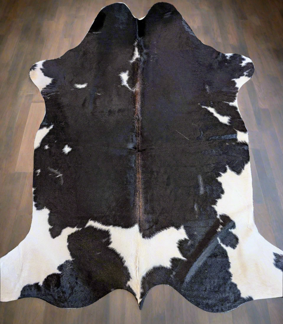 Individually named Kona, a black and white cowhide rug laid out on a wooden floor.
