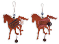 Two rustic metal horse-shaped ornaments side by side. The left ornament has a dark brown label, a small white flower, and a dangling dark brown bell.