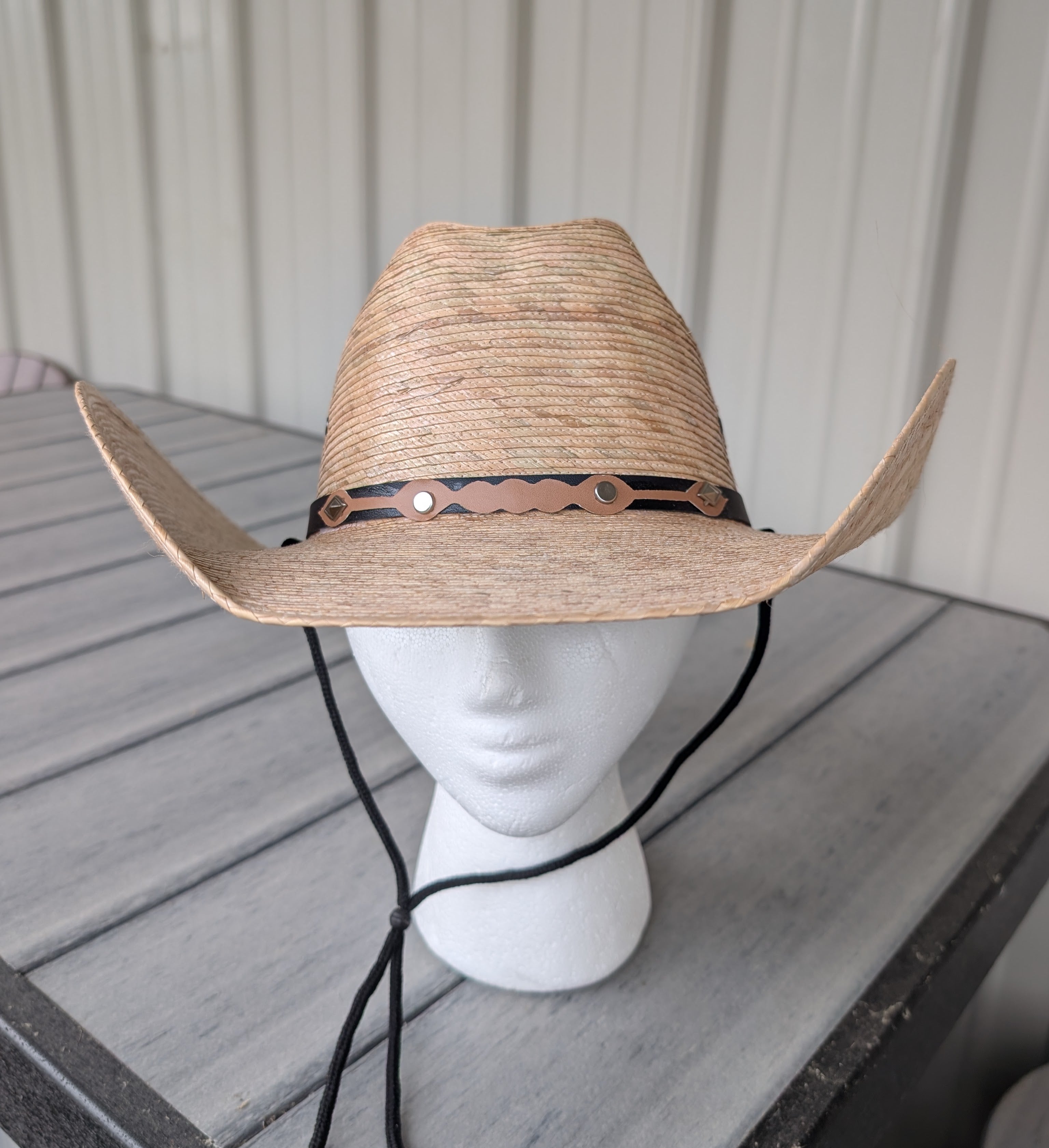 Front view of a dark palm leaf western hat with decorative band and a black stampede string.