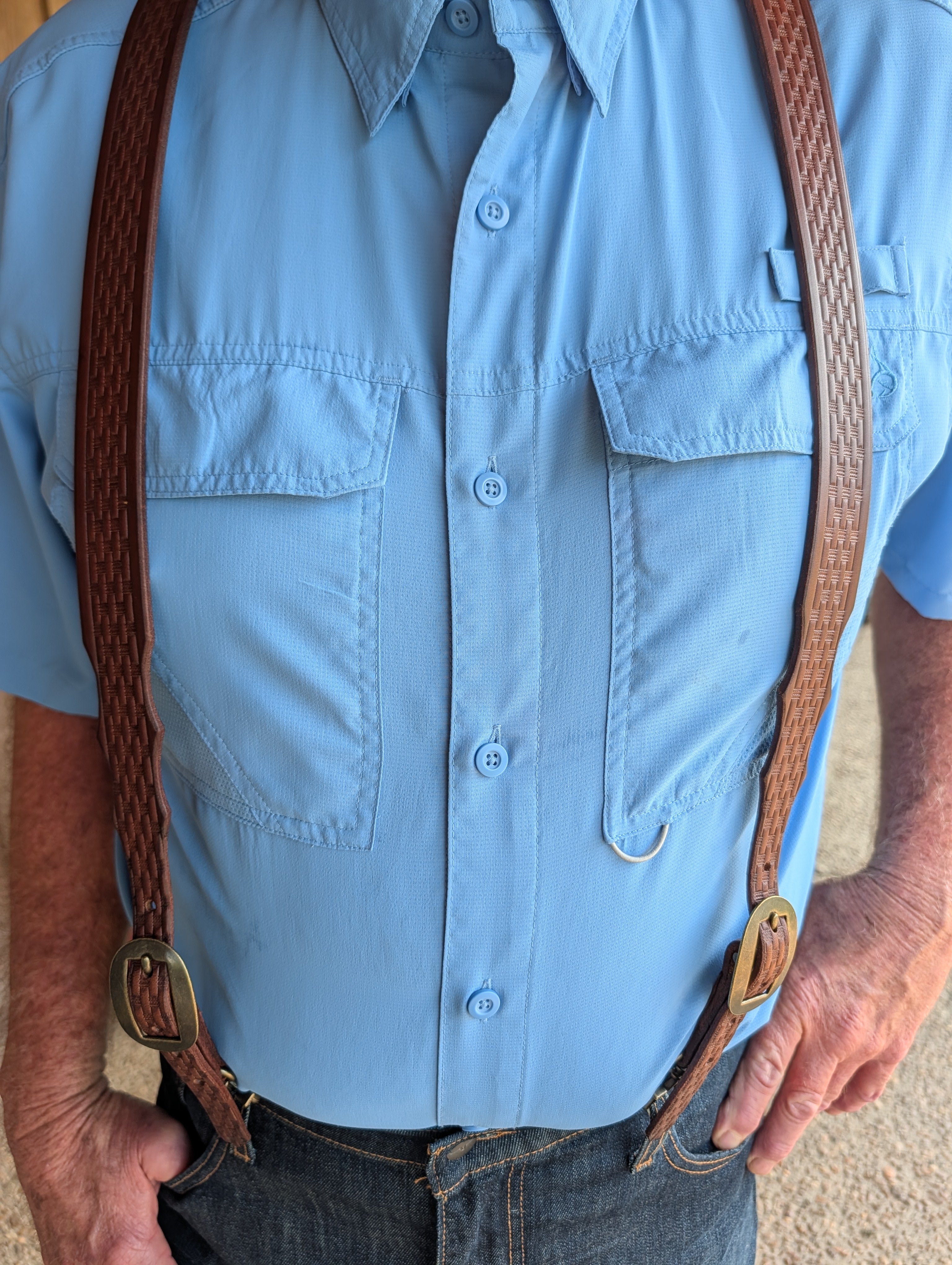 Front view of brown basket stamped genuine bridle leather suspenders worn over a light blue button-down shirt.