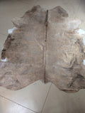 A shimmery blonde colored cowhide with brown spots laid out on the floor.