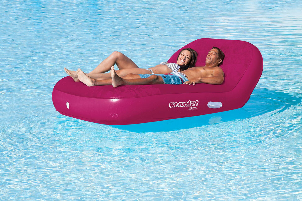 Two people lying on a pink inflatable tube in a pool.