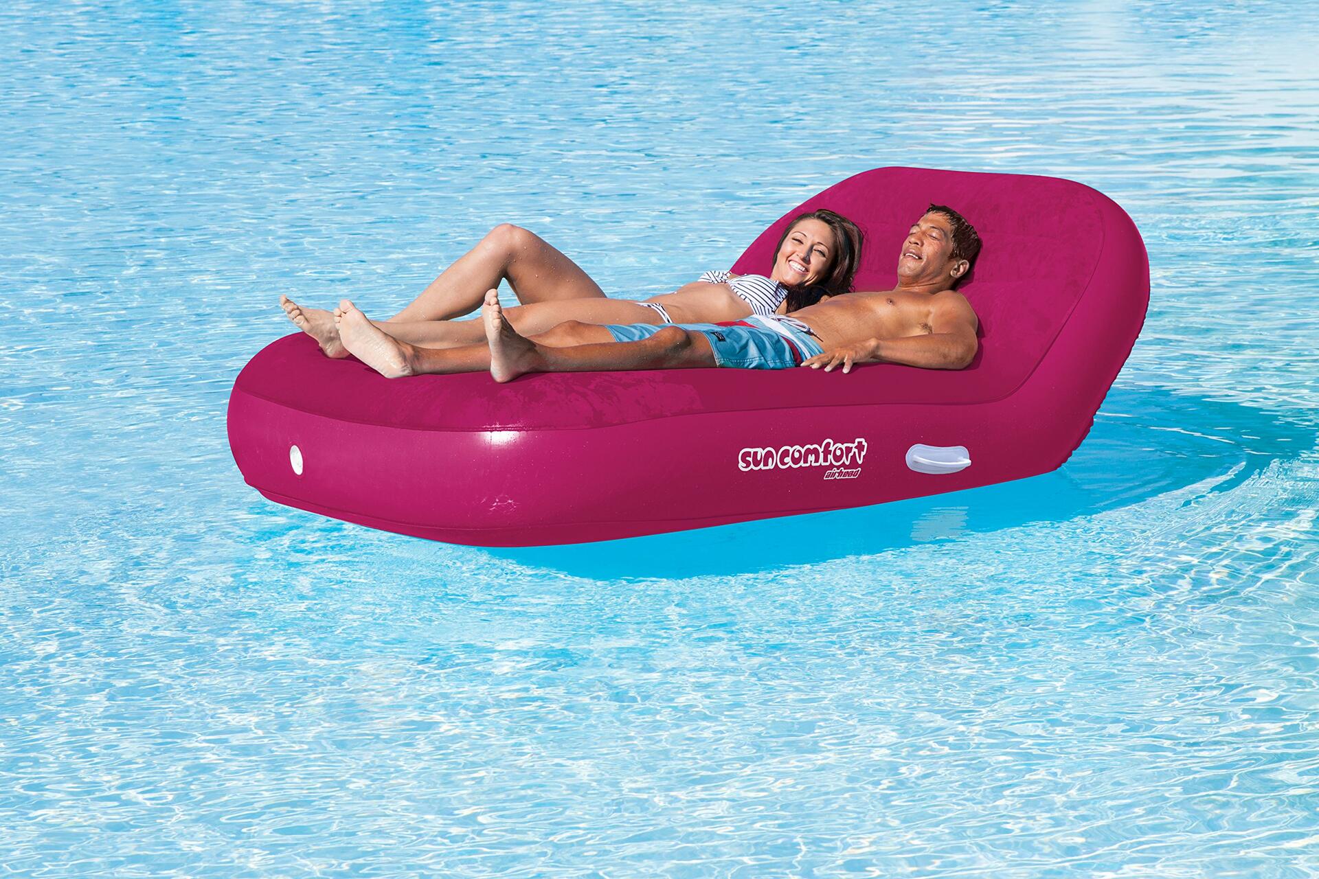 Two people lying on a pink inflatable tube in a pool.