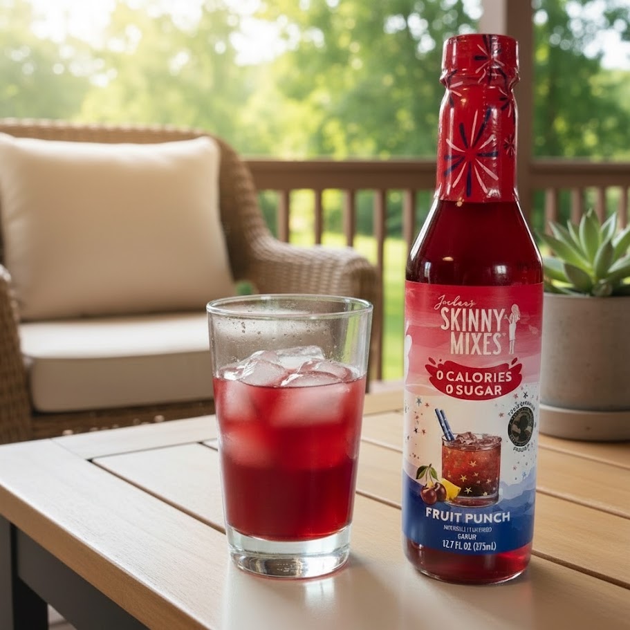 A bottle of Jordan's Skinny Mix in the flavor fruit punch sitting on a table next to a glass with fruit punch and ice, to enjoy outside