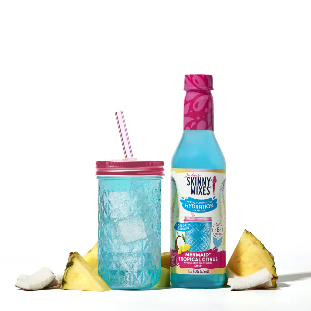 A bottle Jordan's Skinny Mix Mermaid Tropical Citrus Hydration 
375ml next to a glass and pineapple, coconut.