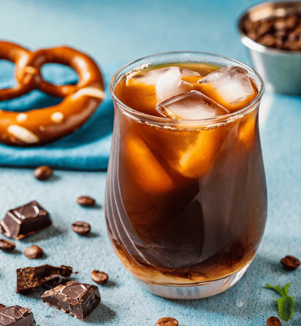 Jordan's Skinny Mix Chocolate Salted Pretzel Syrup flavoring an iced coffee with ice cubes, pretzel, chocolate pieces, and coffee beans.