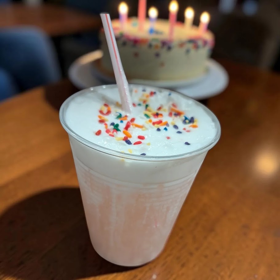 Jordan's Skinny Mix Dippin Dot Birthday Cake Ice Cream flavoring used in a shake with a birthday cake in the background