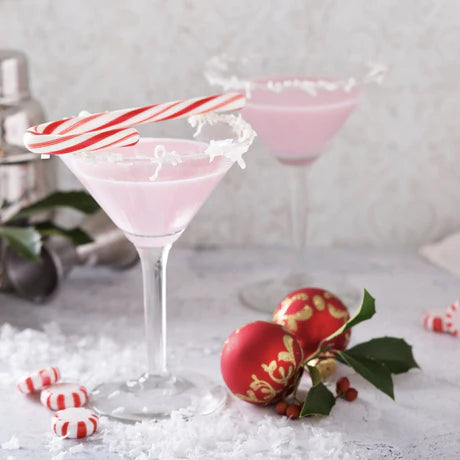 Jordan's Skinny Mix White Chocolate Peppermint Syrup used to flavor a pink cocktail with candy cane garnish on a snowy surface with Christmas decorations.