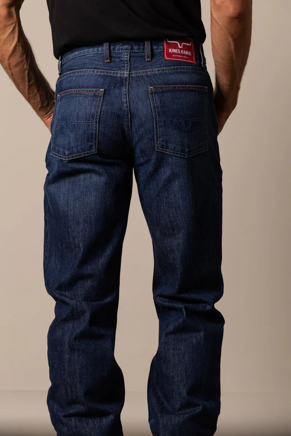 Person wearing Kimes Ranch blue jeans in the style Dillon with a visible brand logo and view on hide pockets.