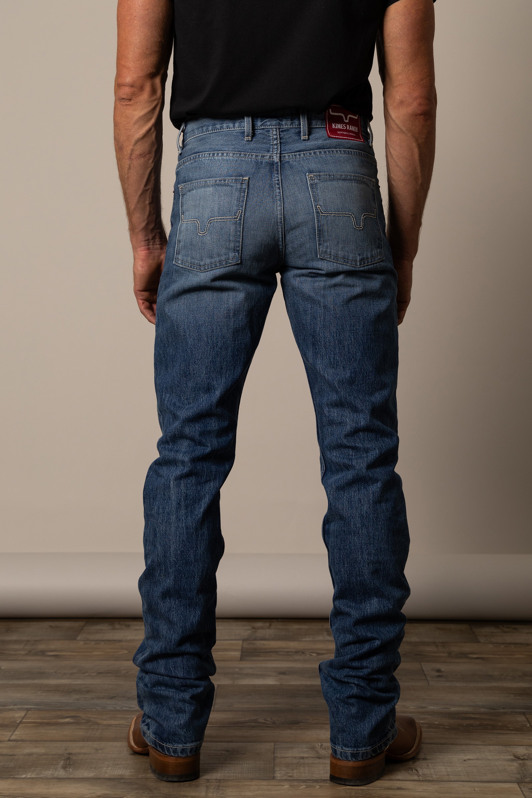Person wearing Kimes Ranch blue jeans showcasing hide pockets and logo label.