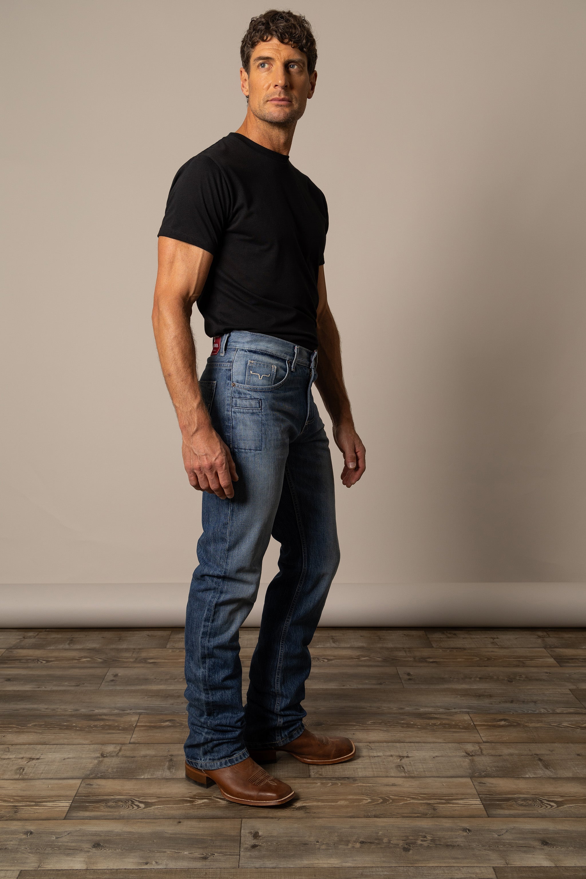 Man wearing a black t-shirt and blue Kimes Ranch jeans in the style James showcasing side view front pockets