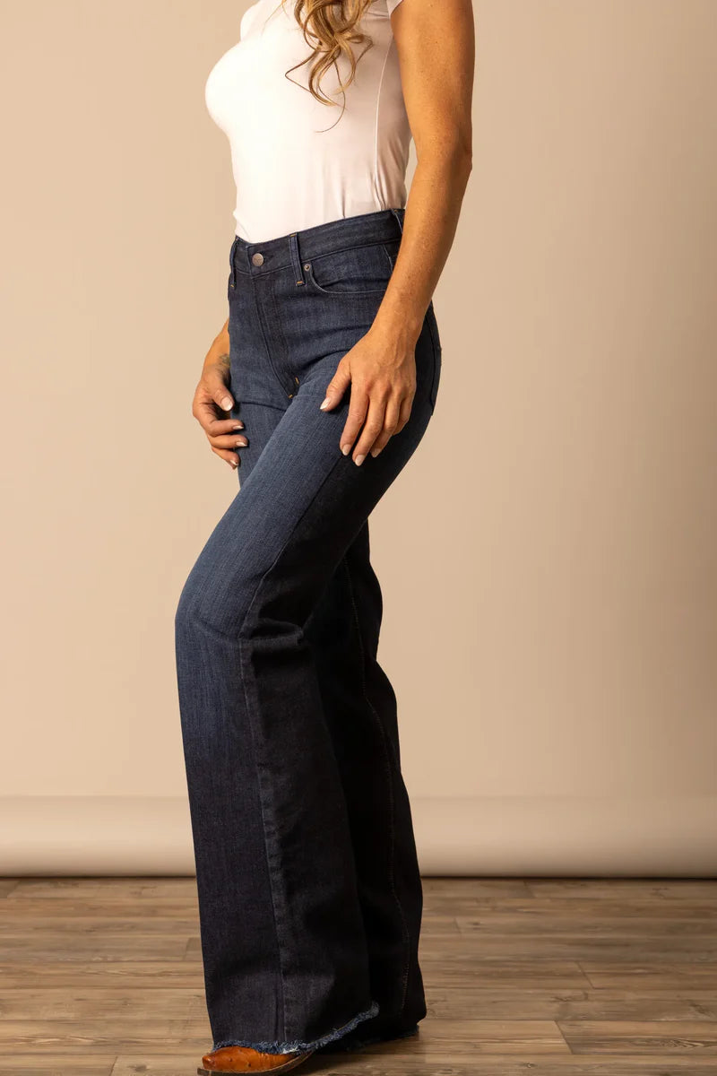 Person wearing Kimes Ranch dark blue jeans and a white top, featuring the flared bottoms and high waist.
