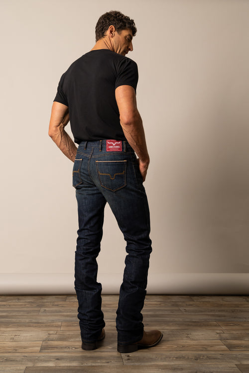 Man wearing Kimes Ranch dark blue jeans in the style Roger and a black t-shirt with a visible brand logo, showcasing hide pockets.