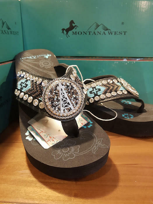 Decorative sandals with rhinestone embellishments on a wooden surface with Montana West box in the background.