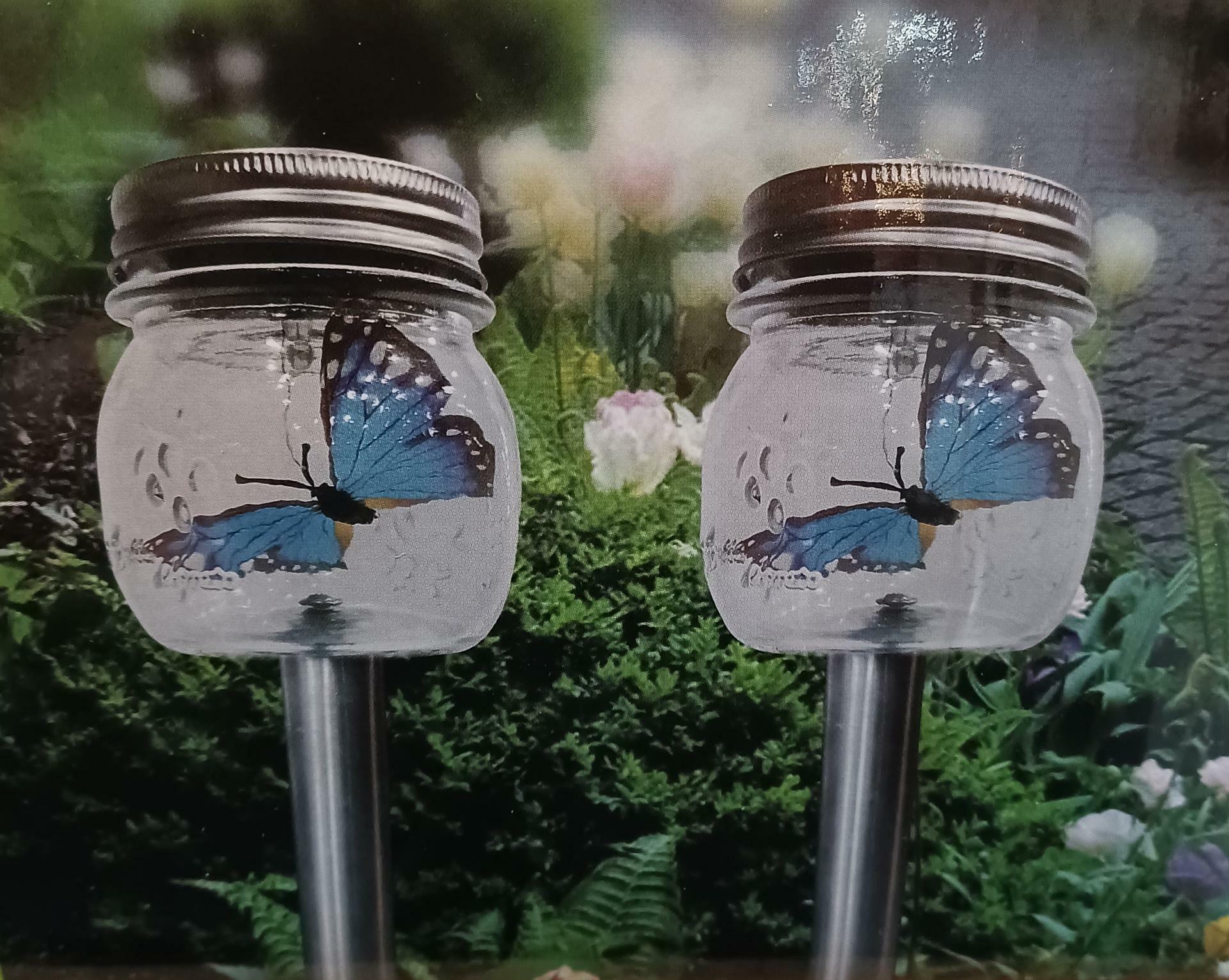 Two clear mason jar lights with butterfly designs on a garden background.
