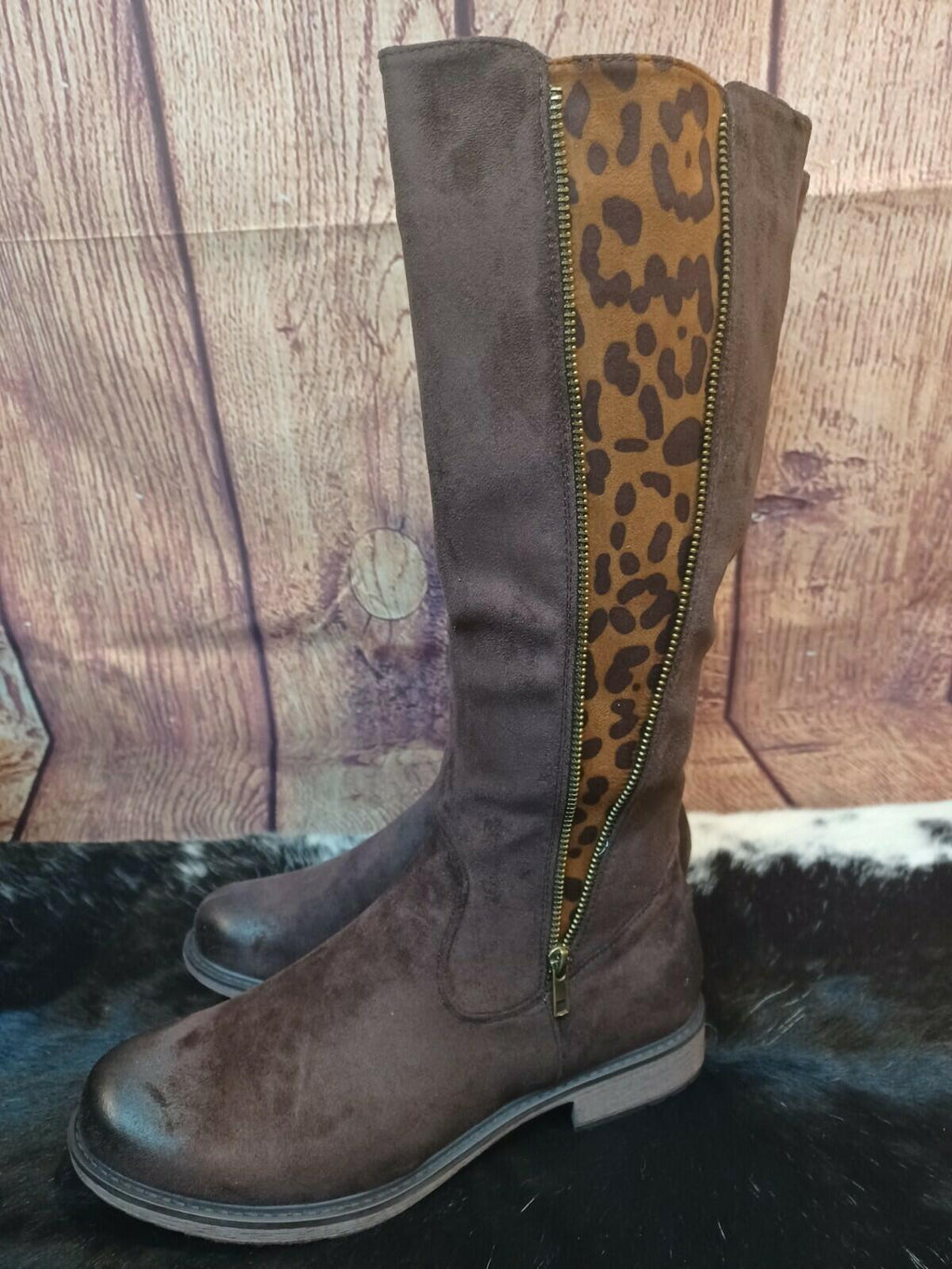 Brown knee-high boot with a leopard print zipper on a wooden floor.