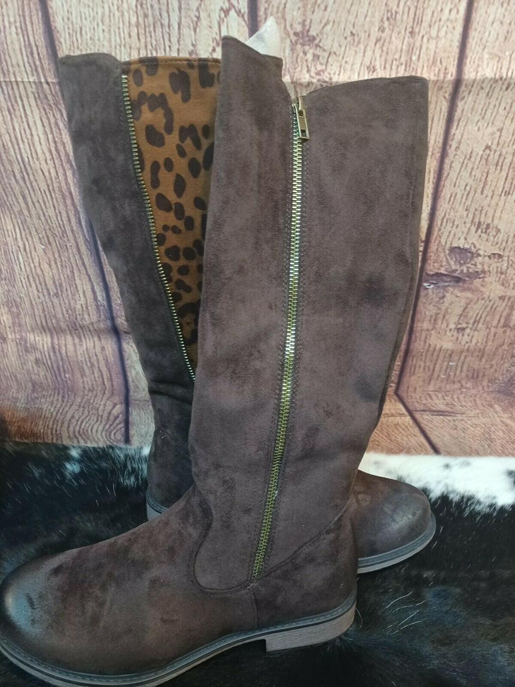 Brown suede knee-high boots with a leopard print interior on a wooden floor.