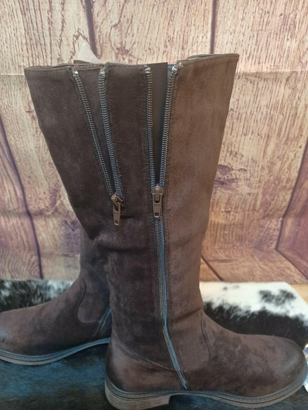 Brown suede knee-high boots with zippers on a wooden surface