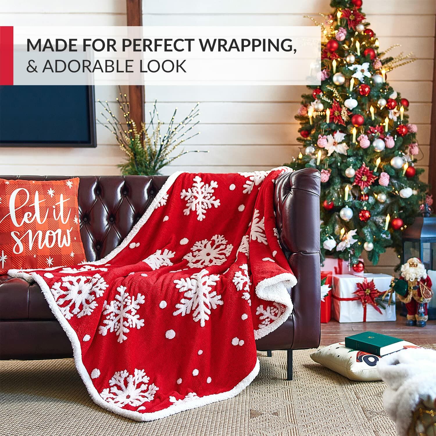 Red blanket with white snowflakes draped over a couch in a festive living room with Christmas tree and presents.