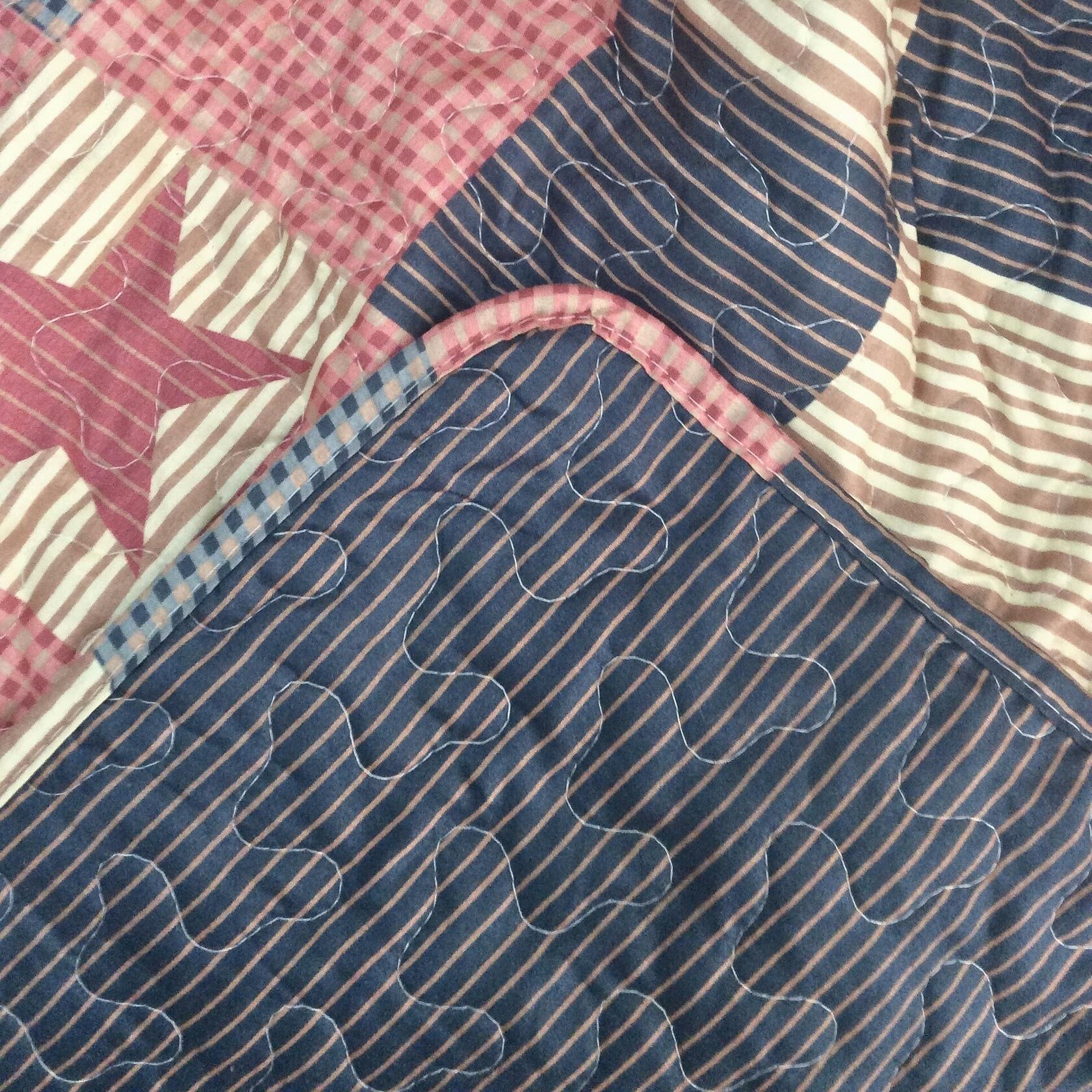 Close-up of a quilt with star and stripe patterns in blue, pink, and beige.