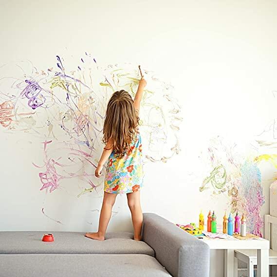 Child painting on a white wall with colorful paint.