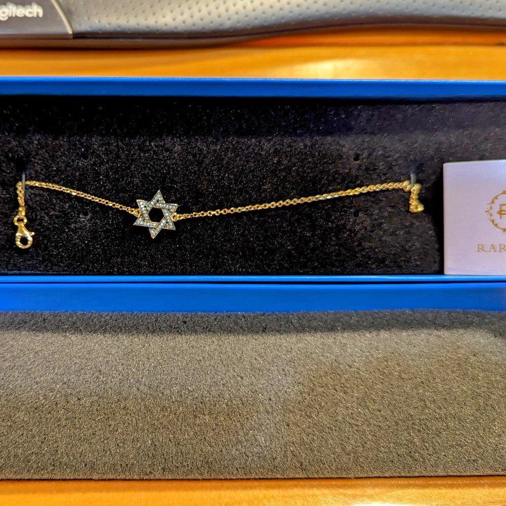 Gold bracelet with a star design on a black display stand.