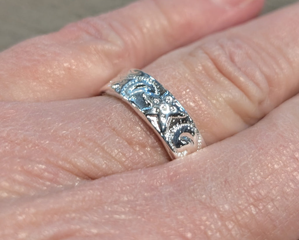 Silver ring with intricate design on a person's finger