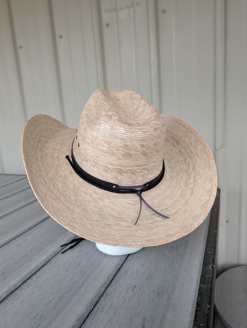 Back view of a light natural palm leaf western hat with a black hat band.