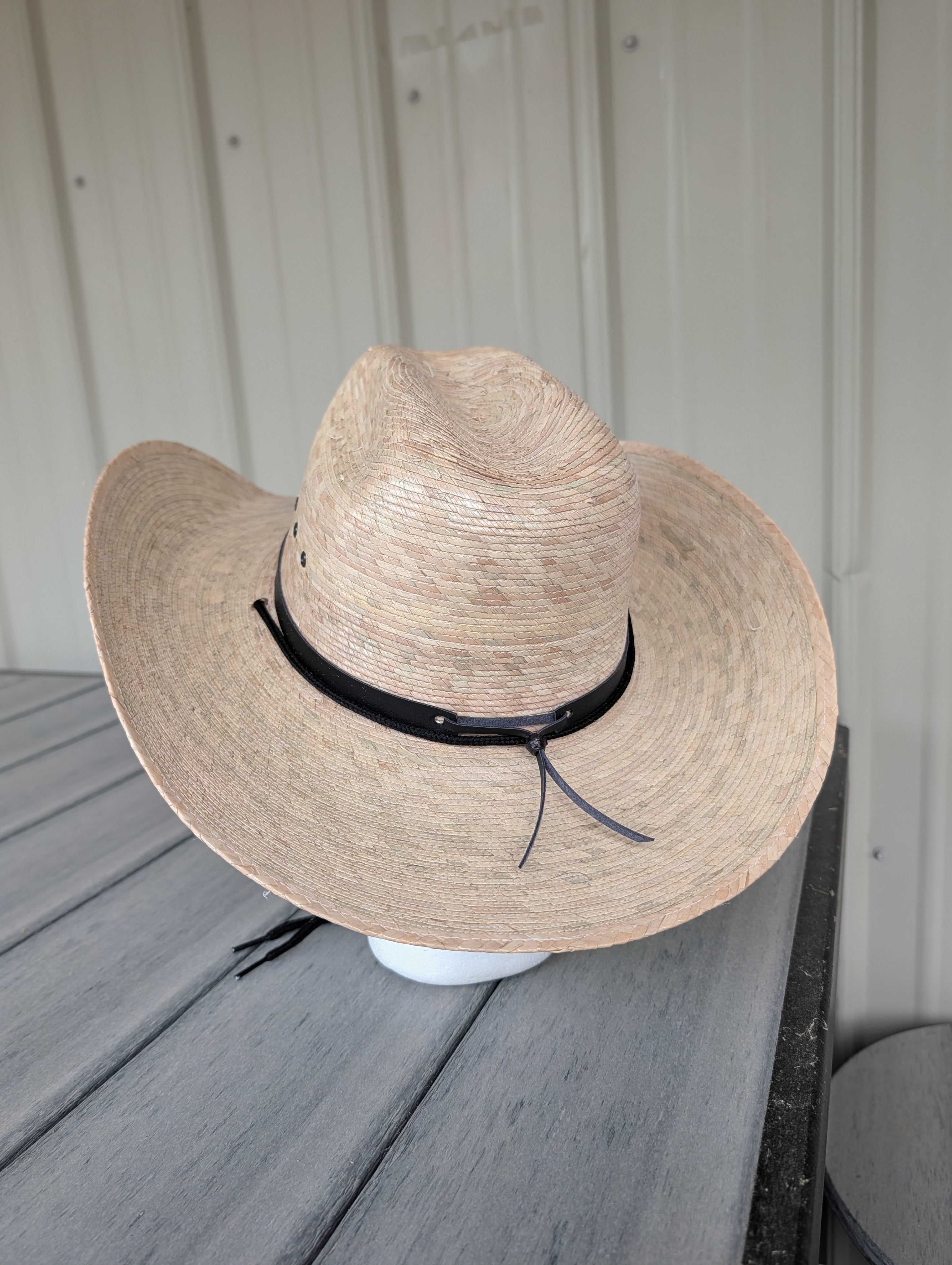 Back view of a light natural palm leaf western hat with a black hat band.