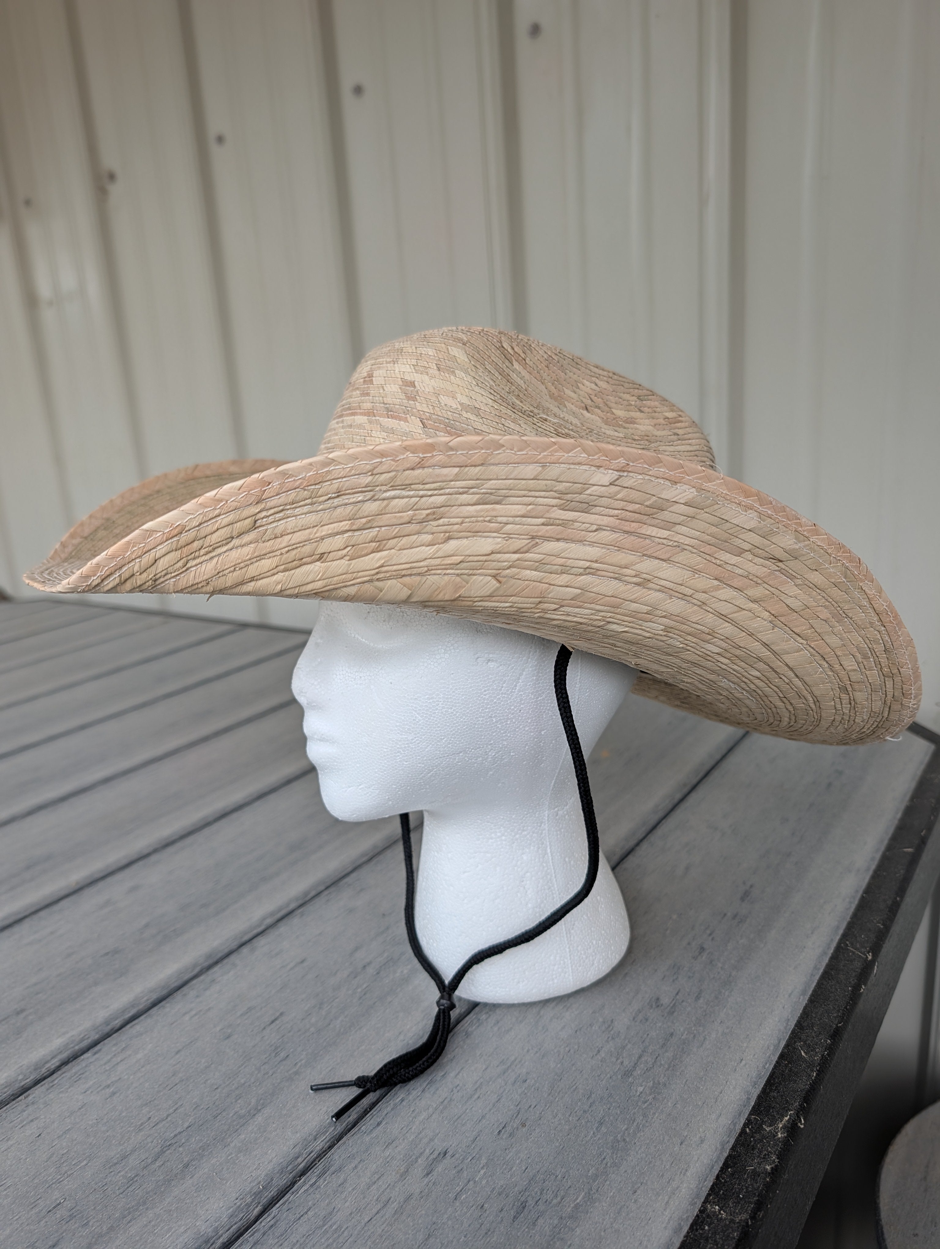 Side view of a light natural palm leaf Western hat with a black stampede string
