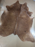 A red and brown cowhide with leopard print-like markings, displayed on a flat surface.