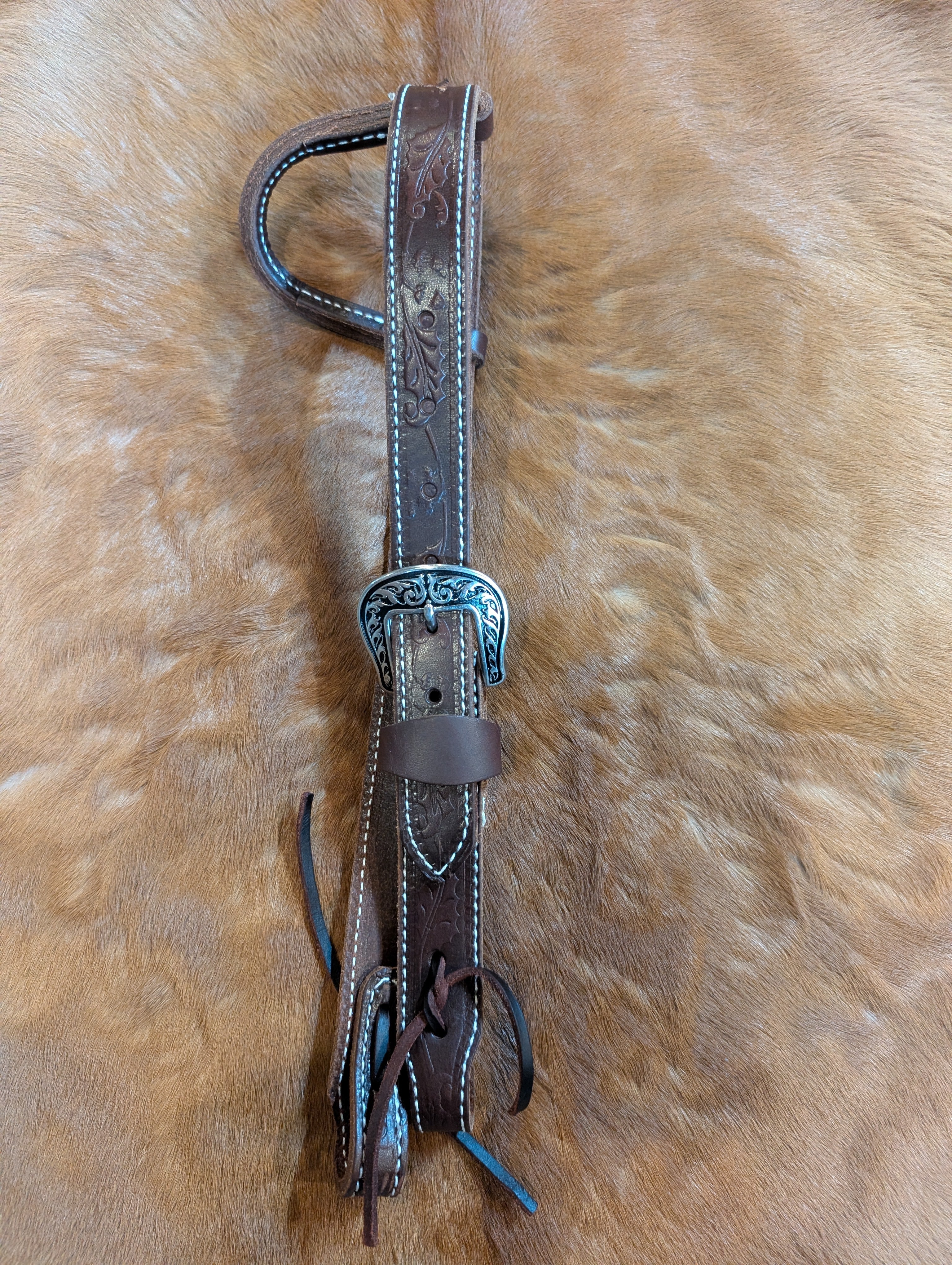 Dark oil leather pony 1-ear Western headstall with acorn leaf tooling and silver buckle, laid on tan cowhide