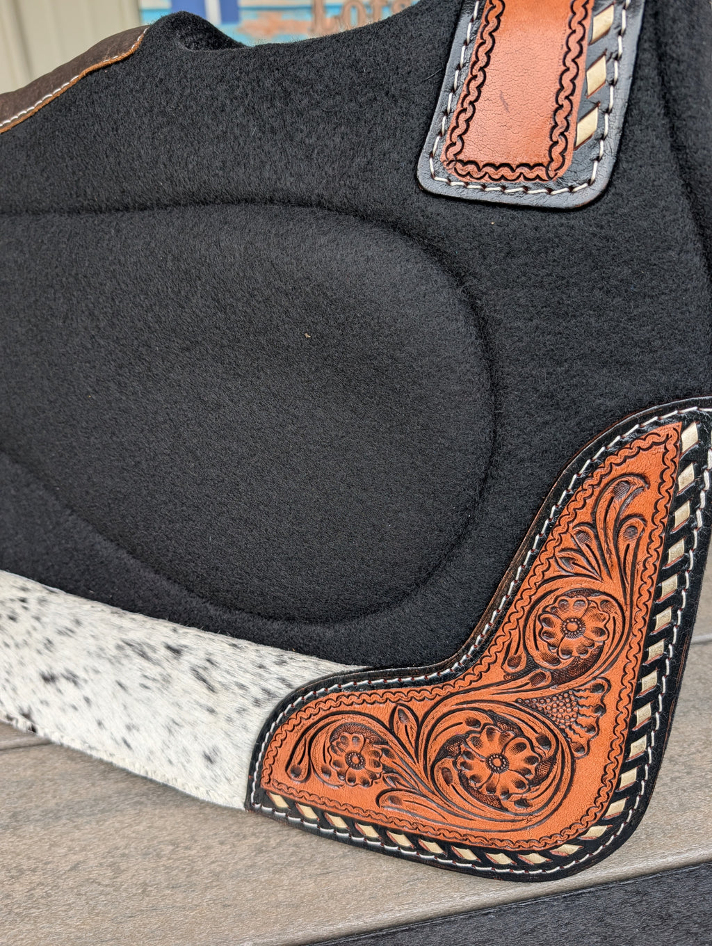 Close-up of a stock yard saddlery built up saddle pad with tooled leather and buckstitched and hairon wear leathers 