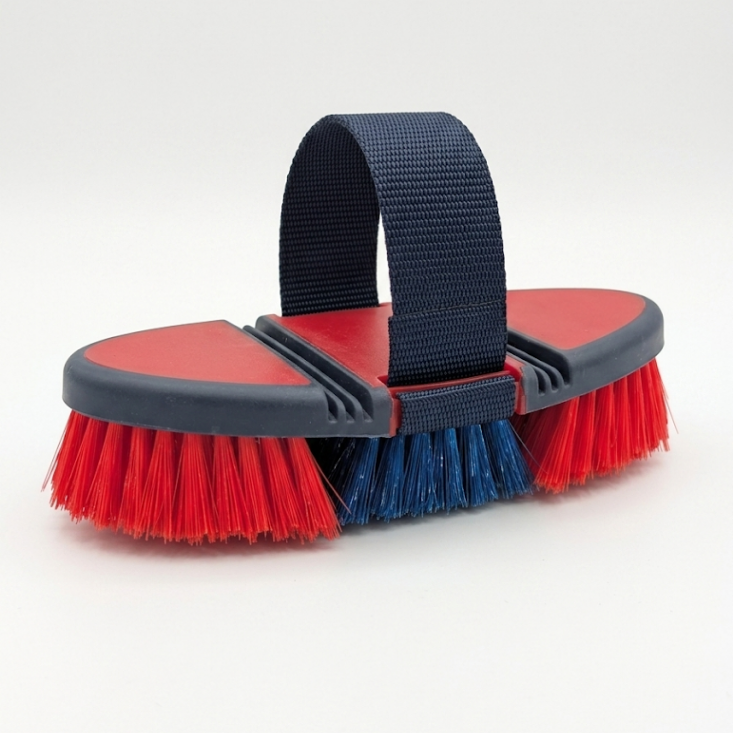 A horse grooming brush with red and blue bristles, a red and gray plastic head, and a navy blue loop handle that adjust s