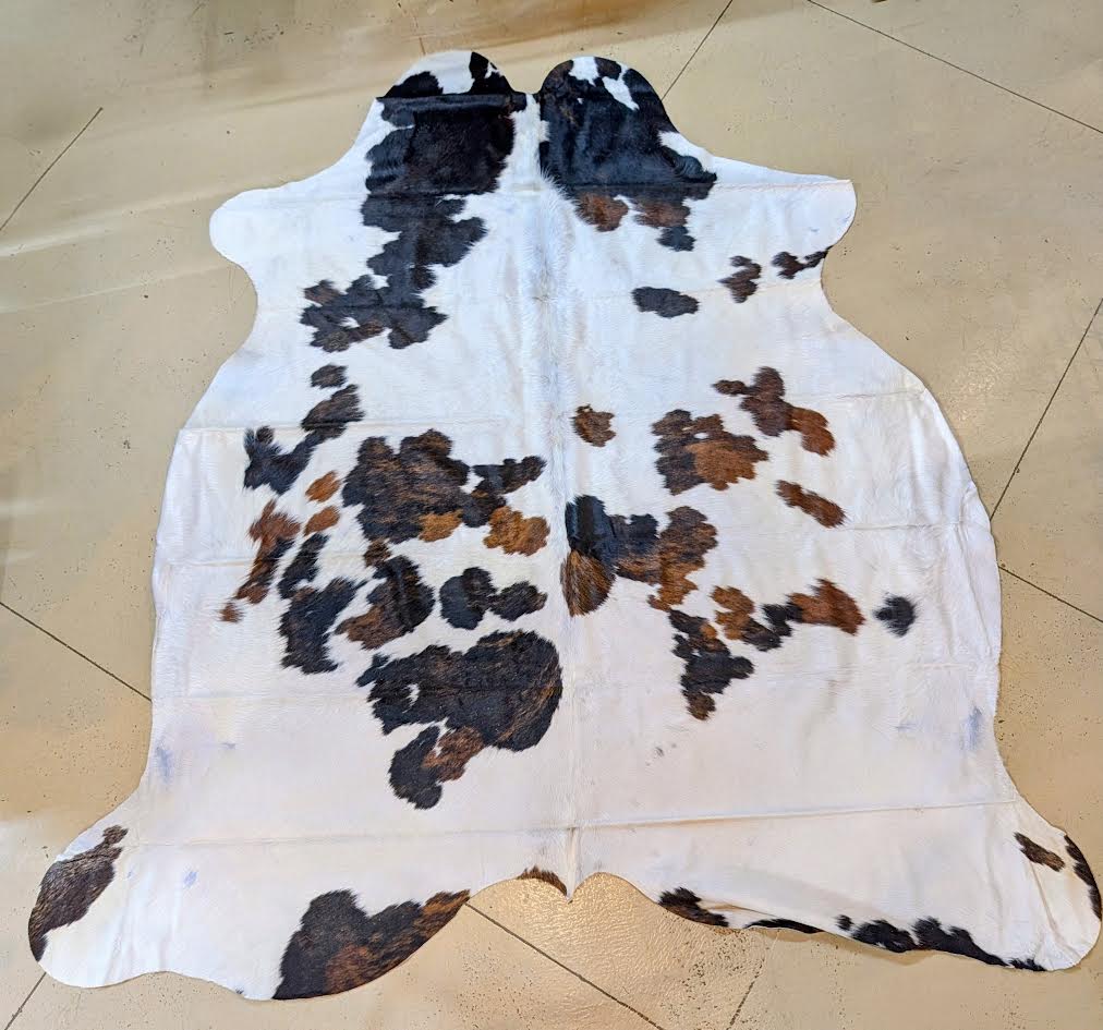 Cowhide rug with black, brown, and white pattern on a tiled floor.